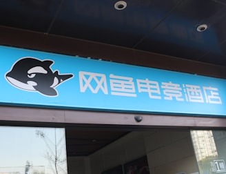 A building entrance features a vibrant blue sign with white Chinese characters and a stylized orca logo in black and white. The overall appearance suggests an establishment focused on eSports or digital activities.