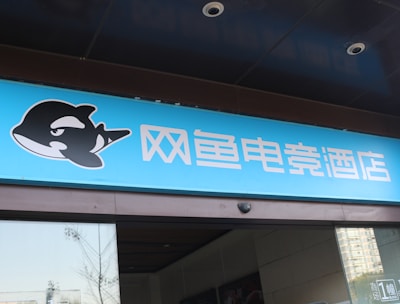 A building entrance features a vibrant blue sign with white Chinese characters and a stylized orca logo in black and white. The overall appearance suggests an establishment focused on eSports or digital activities.